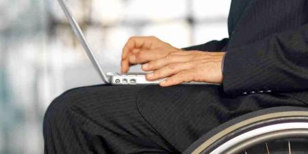 Image of a man wearing a suit, sitting in a wheelchair, and using a laptop computer.