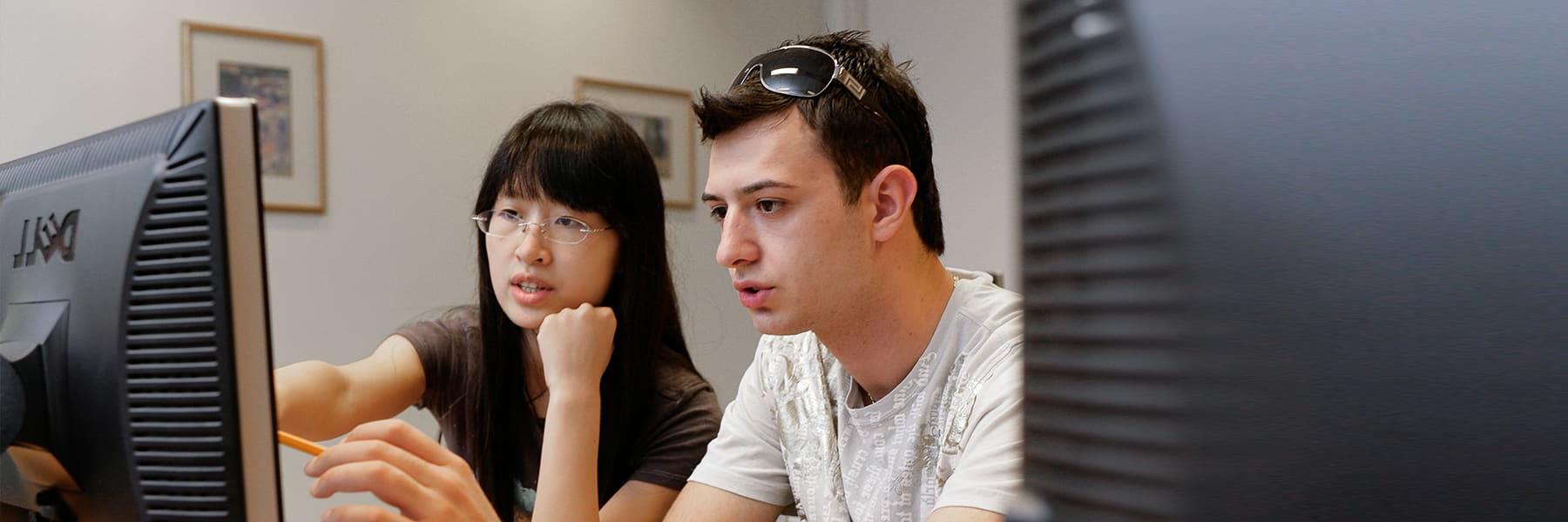 Two students work at a computer helping each other.